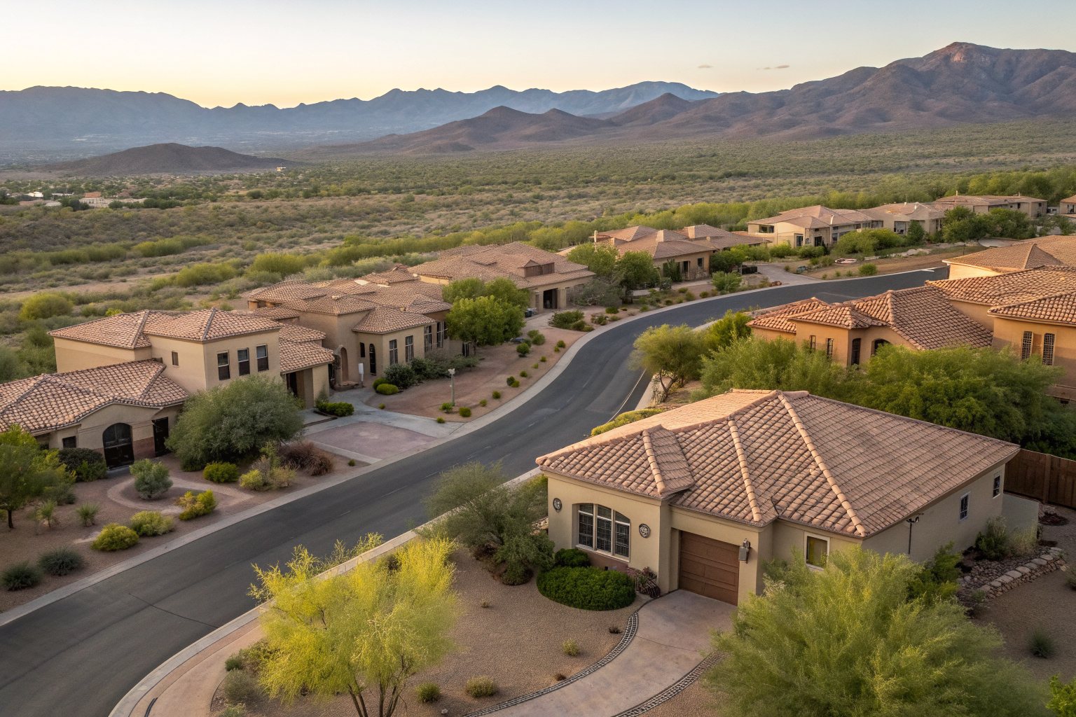 Aerial view of a desert neighborhood of stucco homes with tile roofs along a curving street below mountains